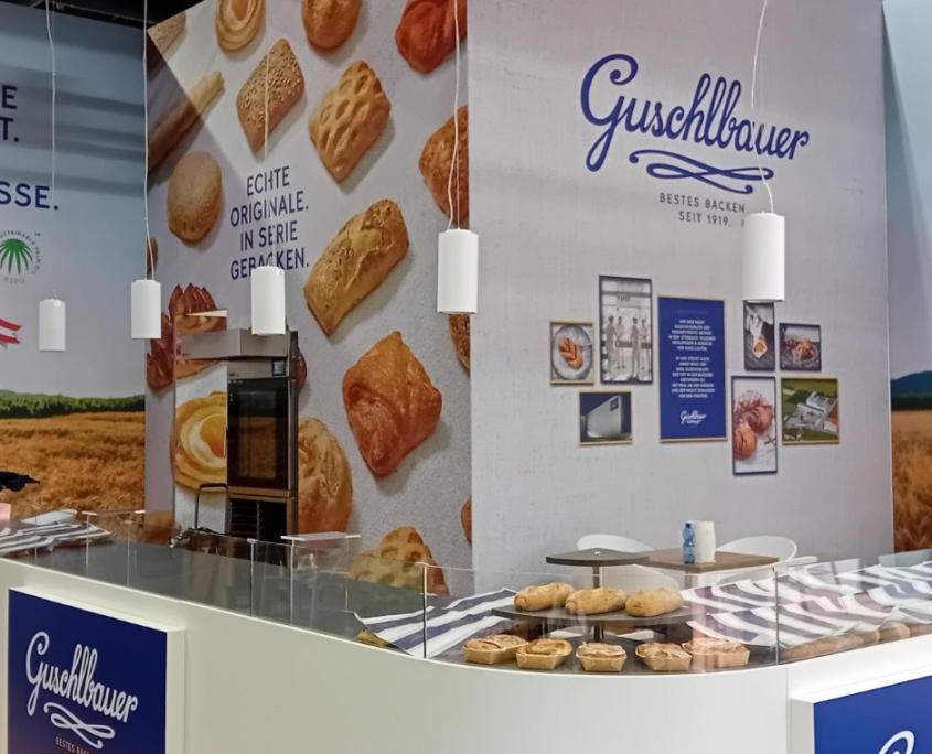 Messestand mit geschwungener Theke mit Sichtglas, integrierte Koje, bedruckte Wände
