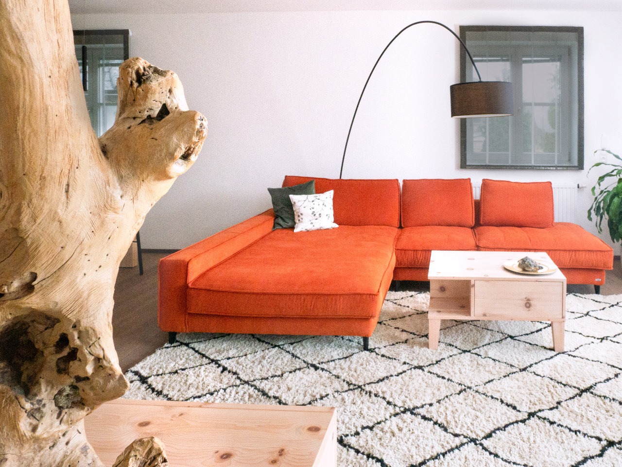 Wohnzimmer mit oranger Couch, geschwungene Lampe, Couchtisch aus Zirbenholz